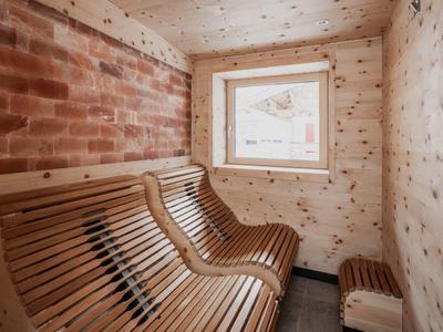 Kleine Holzsauna mit geschwungenen Holzbänken, Fenster und roter Wandverkleidung.