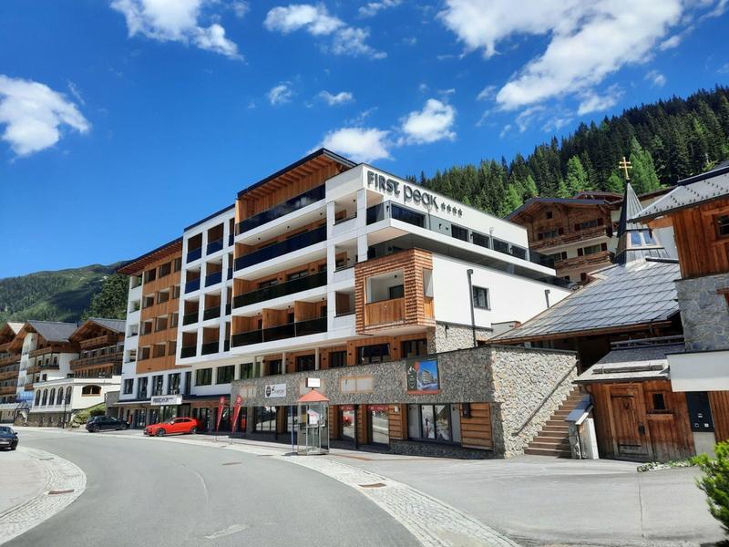 Mehrstöckiges Hotelgebäude mit großem Schriftzug in alpiner Landschaft unter blauem Himmel.