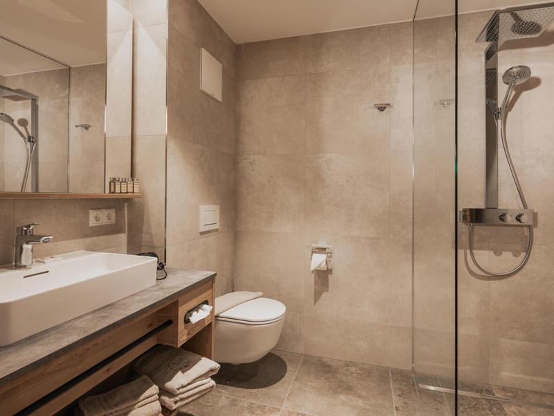 Modernes Badezimmer mit heller Holzkommode, großem Spiegel und ebenerdiger Dusche mit Glasabtrennung.