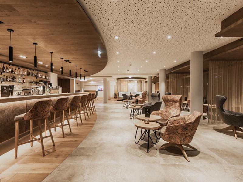 Moderne Bar mit warmem Licht, Lederstühlen und einer runden Holztheke in hellem Interieur.