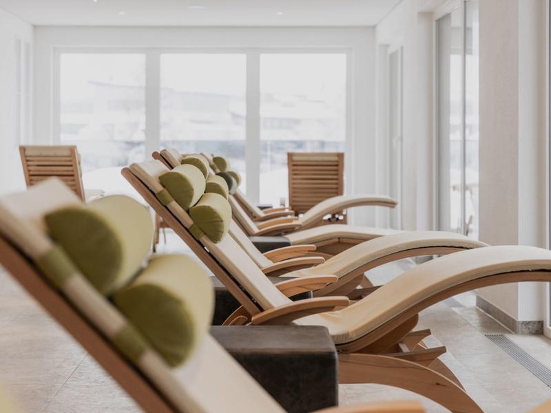 Moderne Ruheliegen mit Kissen in einem hellen Wellnessraum mit großen Fensterfronten.