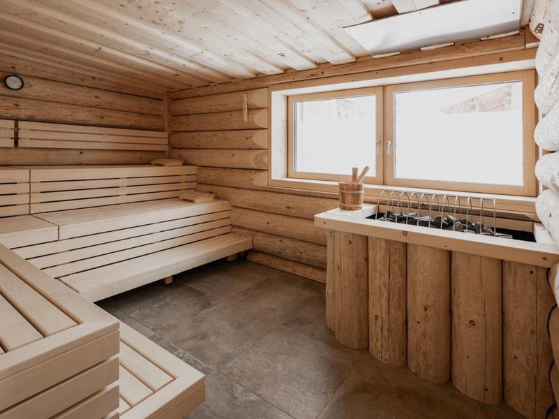 Helle Holzsauna mit Fenster, mehrstufigen Bänken und Saunaofen aus Holzverkleidung.