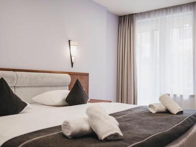 Modern hotel room with large bed, white linens, and rolled towels.