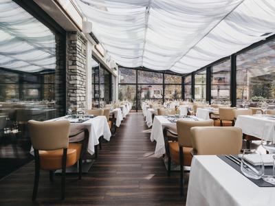 Elegant restaurant with white tablecloths and beige chairs under a transparent roof.