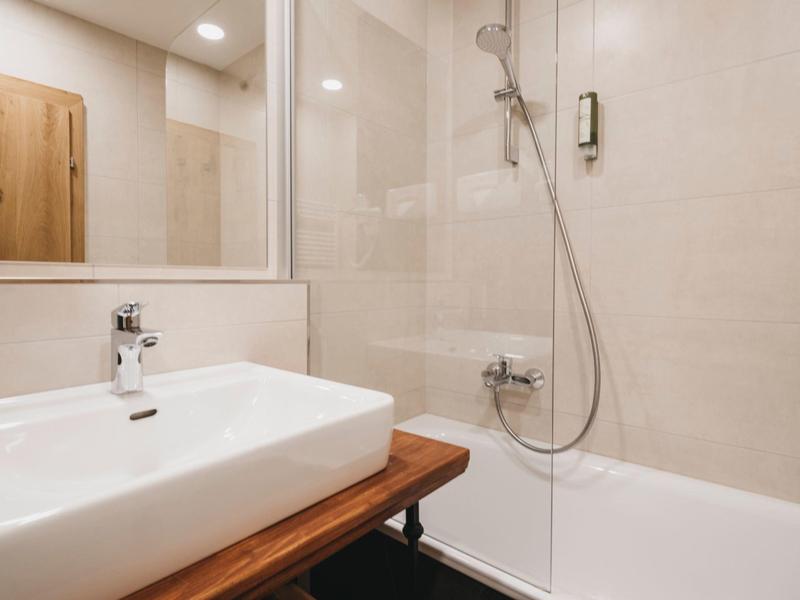 Salle de bain moderne avec lavabo, grand miroir et baignoire avec paroi de douche.