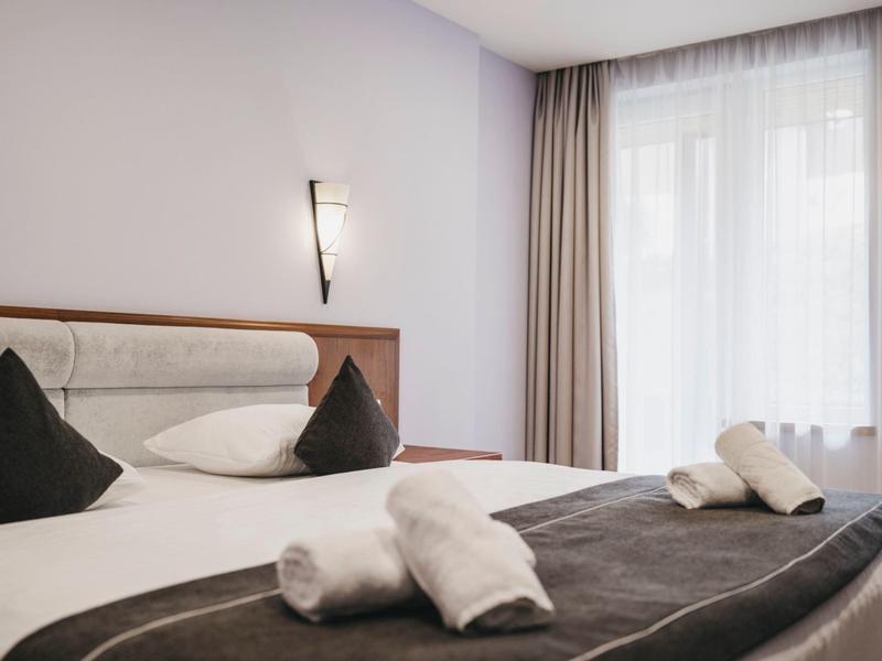 Chambre d'hôtel moderne avec un lit, des oreillers blancs et noirs, une table de chevet et une grande fenêtre avec des rideaux.