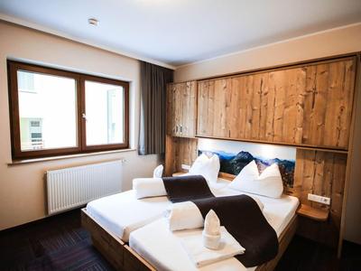 Gemütliches Schlafzimmer mit Holzmöbeln, Doppelbett, weißen Kissen und Decken, Fenster und Vorhängen.