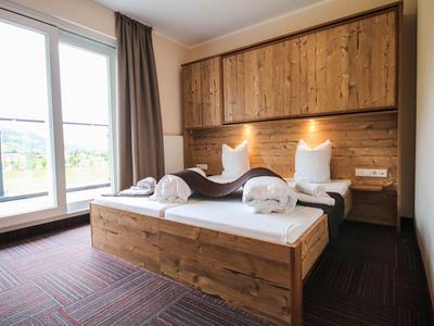 Helles Schlafzimmer mit Holzmöbeln, großem Bett, zwei weißen Handtüchern und bodentiefem Fenster.