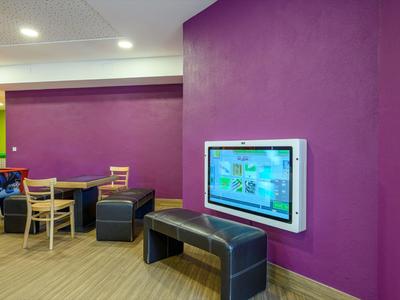 Moderner Aufenthaltsraum mit lila Wänden, Sitzmöbeln und einem Wandbildschirm.