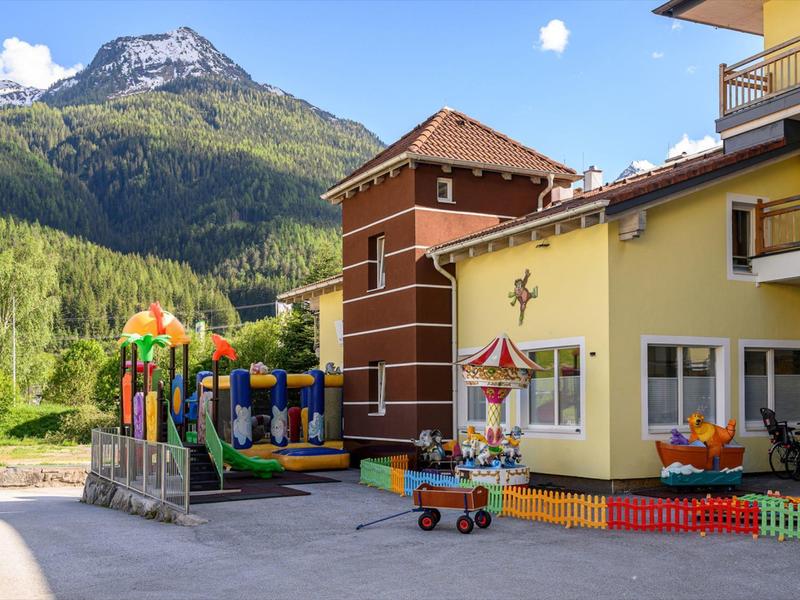 Bunten Kinderspielplatz vor einem gelben Gebäude mit Bergen im Hintergrund.