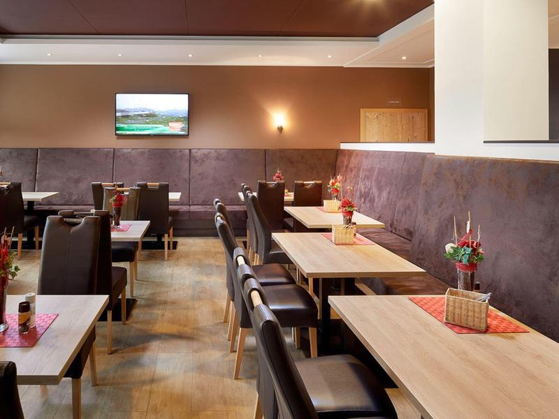 Gemütlicher Speisesaal mit Holztischen, schwarzen Stühlen und Wanddekorationen.