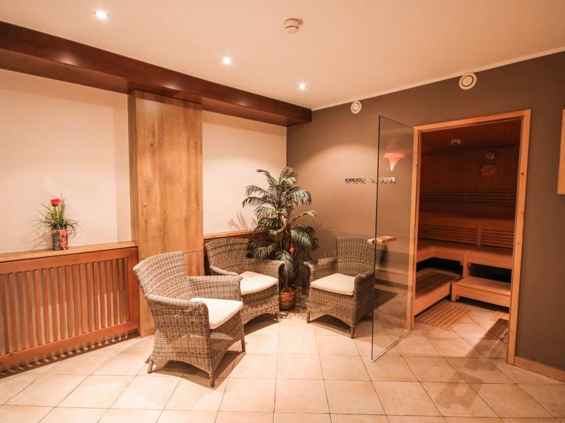 Gemütlicher Saunabereich mit zwei hellen Korbsesseln, Pflanzen und holzvertäfelter Sauna.