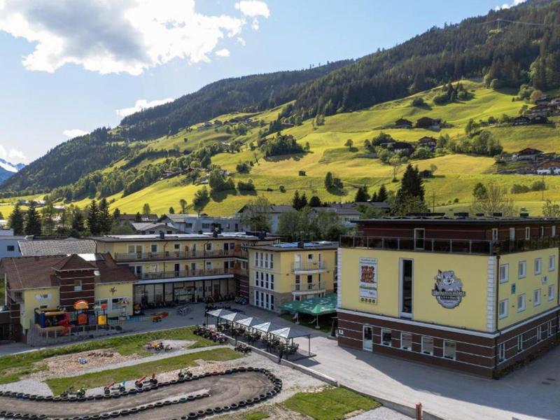 Hotelgebäude am Fuße grüner, sonniger Berge mit klaren Himmel.