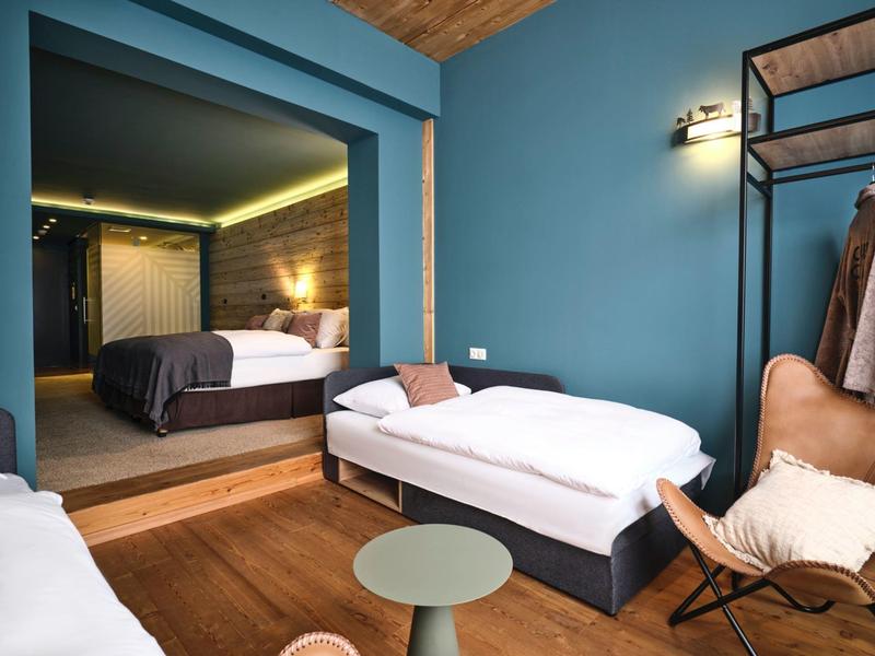 Modernes Schlafzimmer mit zwei Betten, blau-grünen Wänden, Holzdecke und schlichtem Möbelstil.