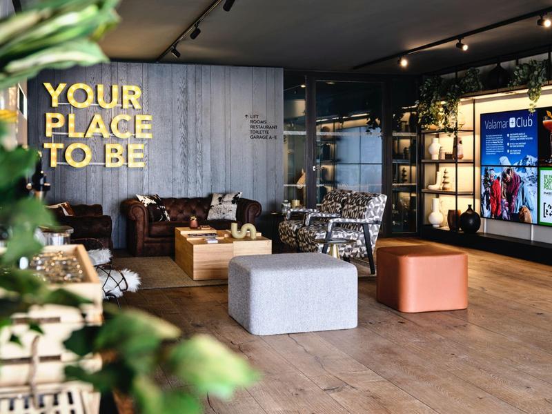 Moderne Lounge mit gemütlichen Sesseln, Couchtischen, Holzboden und leuchtendem Schriftzug.