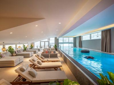 Piscina interna moderna con lettini e grandi finestre luminose.