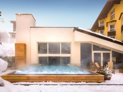 Piscina esterna riscaldata circondata dalla neve davanti a un hotel moderno.