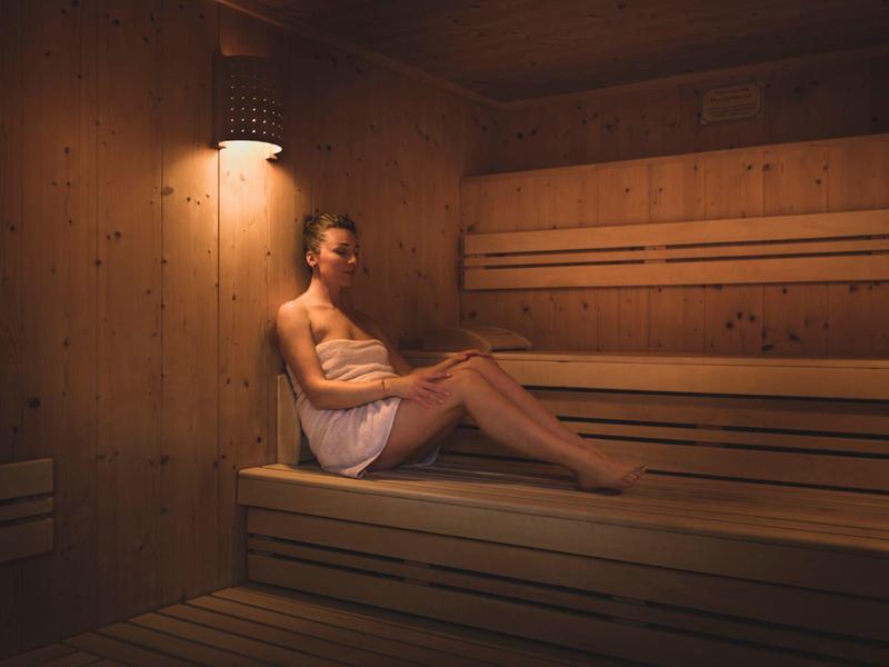 Uomo seduto rilassato in una sauna di legno con luce soffusa.