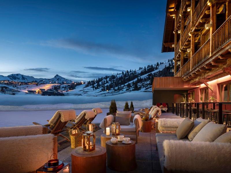 Terrasse d'hôtel avec sièges confortables face à un paysage montagneux enneigé au crépuscule.