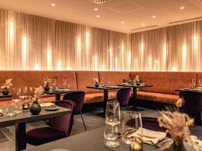 Ristorante elegante con tavoli apparecchiati, sedie imbottite e illuminazione calda alle pareti.