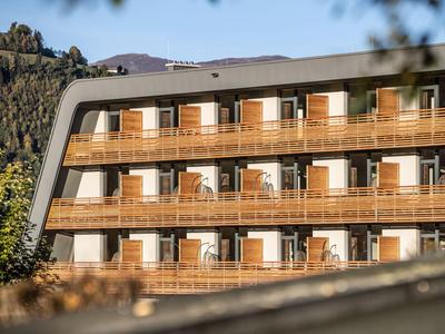 Complesso alberghiero moderno con facciata in legno in un paesaggio montano soleggiato.