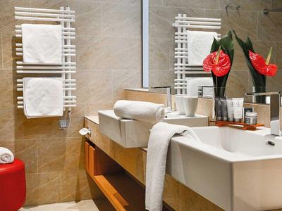 Bagno moderno con grande specchio, lavabo bianco, asciugamani e fiori rossi.