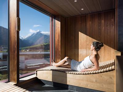 Donna rilassata su panca in legno vicino a finestra panoramica con vista montagna.