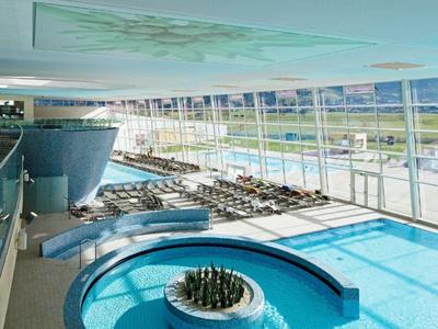 Vista interna di una piscina coperta moderna con grandi finestre in vetro e vista esterna.