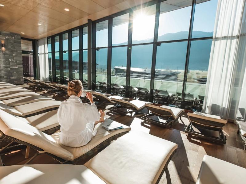 Donna in accappatoio si rilassa su una sdraio nell'area spa con vista panoramica sul mare.