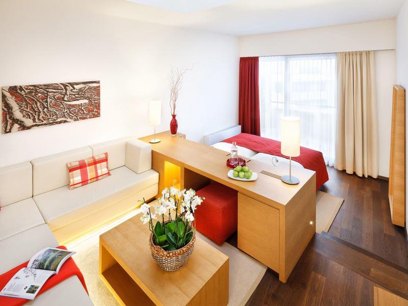 Soggiorno luminoso con divano beige, mobili in legno e grande finestra con tende.