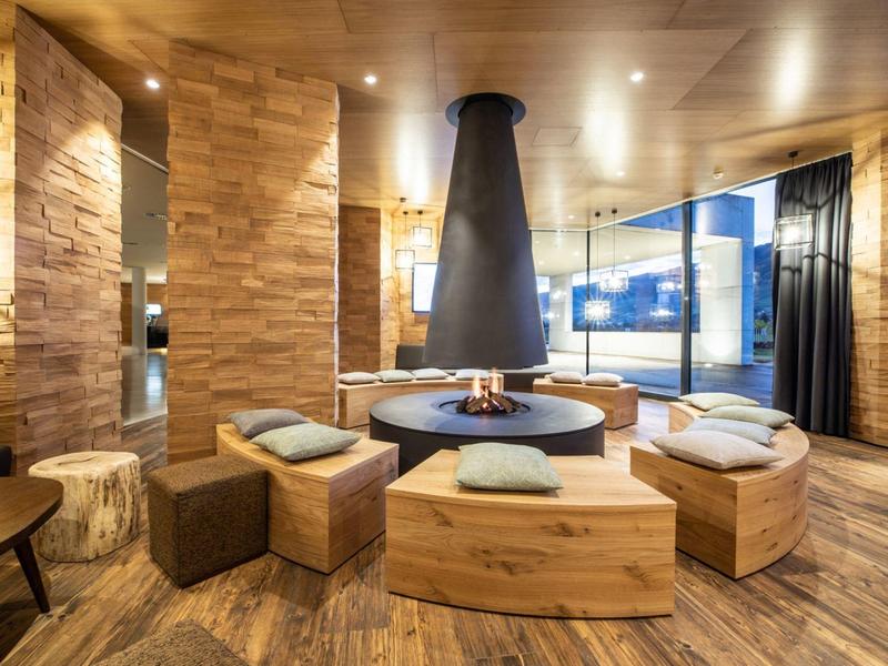 Accogliente area lounge dell'hotel con camino centrale e interno in legno.