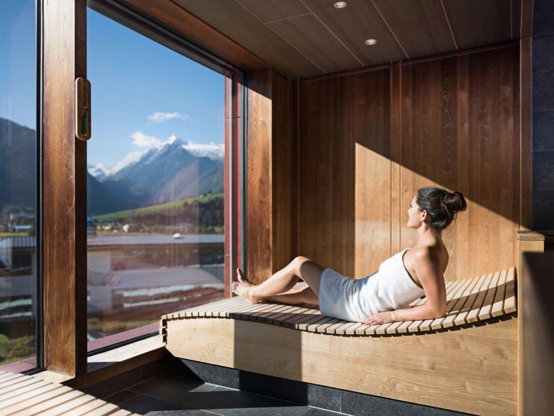 Donna rilassata su panca in legno vicino a finestra panoramica con vista montagna.