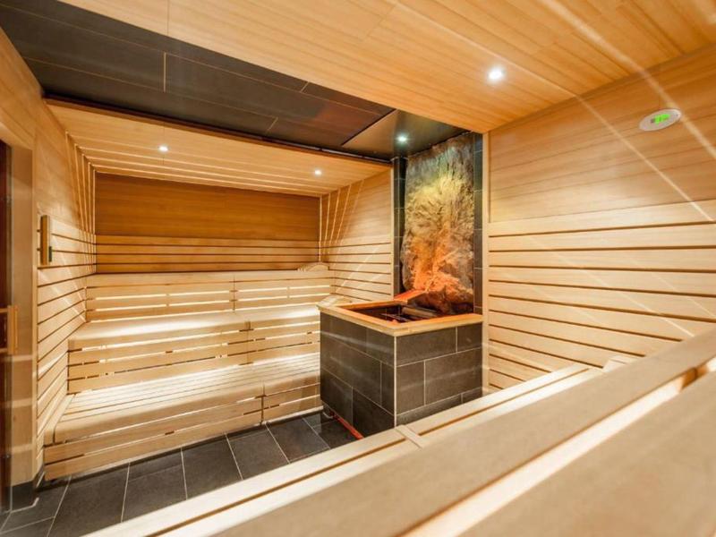Vista interna di una sauna moderna in legno con panche a più livelli e stufa in pietra.