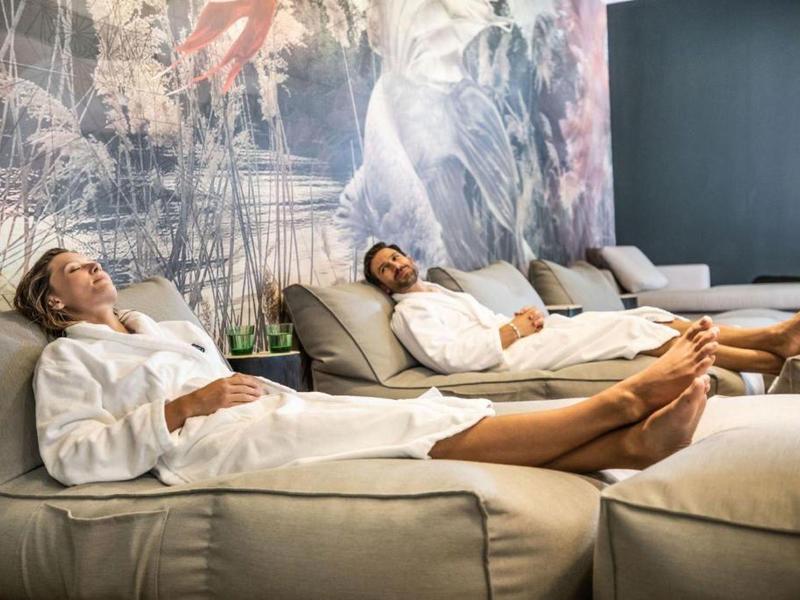 Due persone si rilassano in accappatoi bianchi su lettini in un centro benessere.