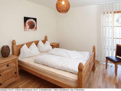 Camera da letto luminosa con letto in legno, comodini e una sedia accanto a una finestra con tende verticali.