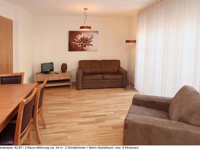 Soggiorno luminoso con divani marroni, pavimento in legno e scrivania con computer.