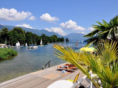Výhled na jezero s lehátky, molem a palmami pod modrou oblohou.
