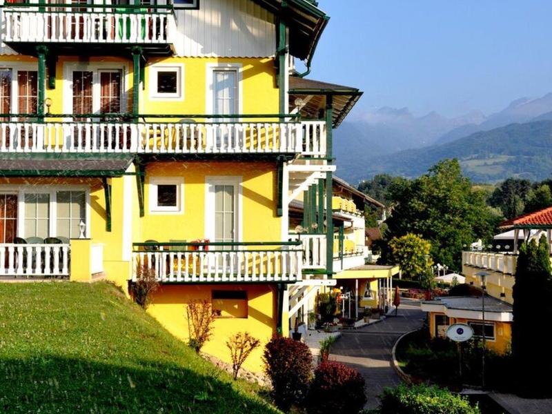 Žlutý vícepatrový hotel s balkony na pozadí horské krajiny a jasně modré oblohy.