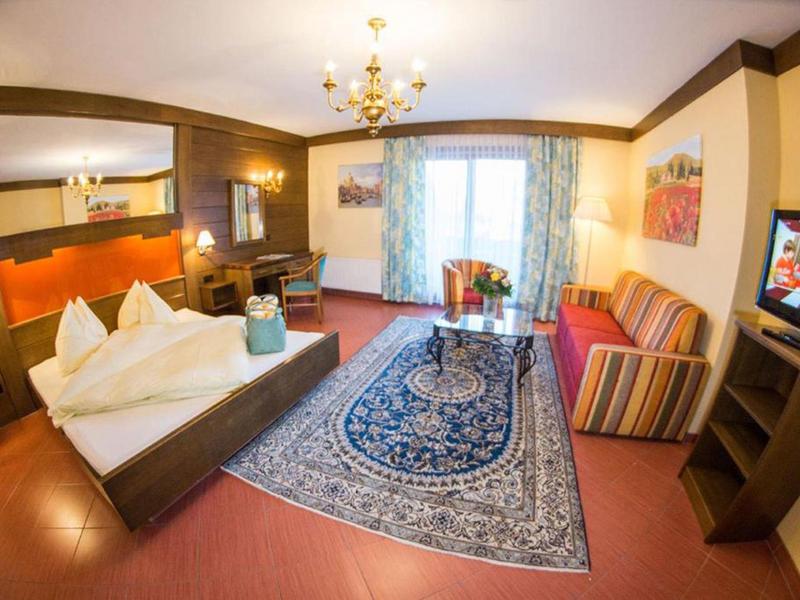 Pohodlný hotelový pokoj s manželskou postelí, kobercem, pohovkou a balkonem s závěsy.