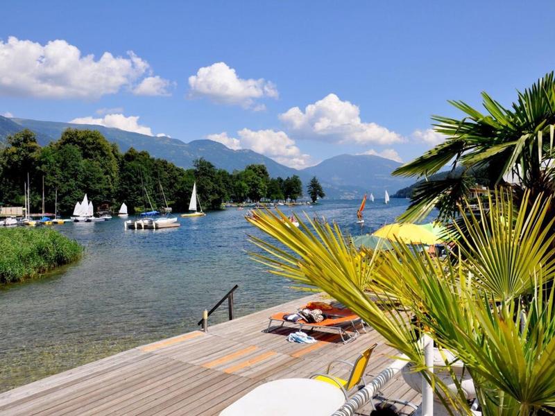 Výhled na jezero s lehátky, molem a palmami pod modrou oblohou.