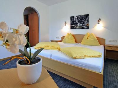 Bright hotel room with double bed, yellow bedding, wooden furniture, and a white orchid on the table.