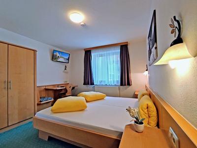 Cozy hotel room with a double bed, yellow pillows, wooden furniture, and a window with curtains.