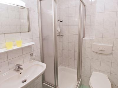 Small hotel bathroom with white tiles, a sink, glass shower, and toilet.