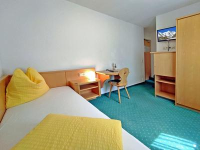 Cozy hotel room with single bed, yellow pillows, desk, chair, and wardrobe on green carpet.