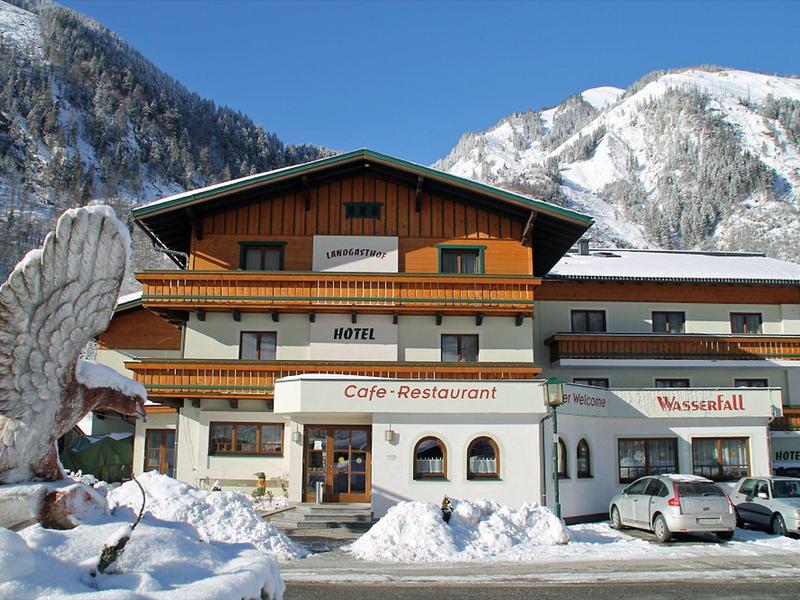 Chalet-style hotel with snow and mountain backdrop, eagle sculpture in foreground.