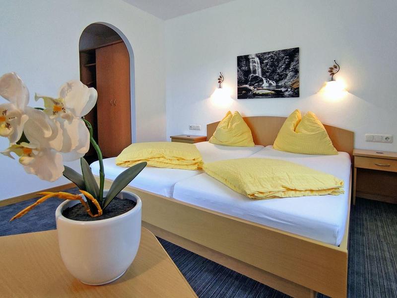 Bright hotel room with double bed, yellow bedding, wooden furniture, and a white orchid on the table.