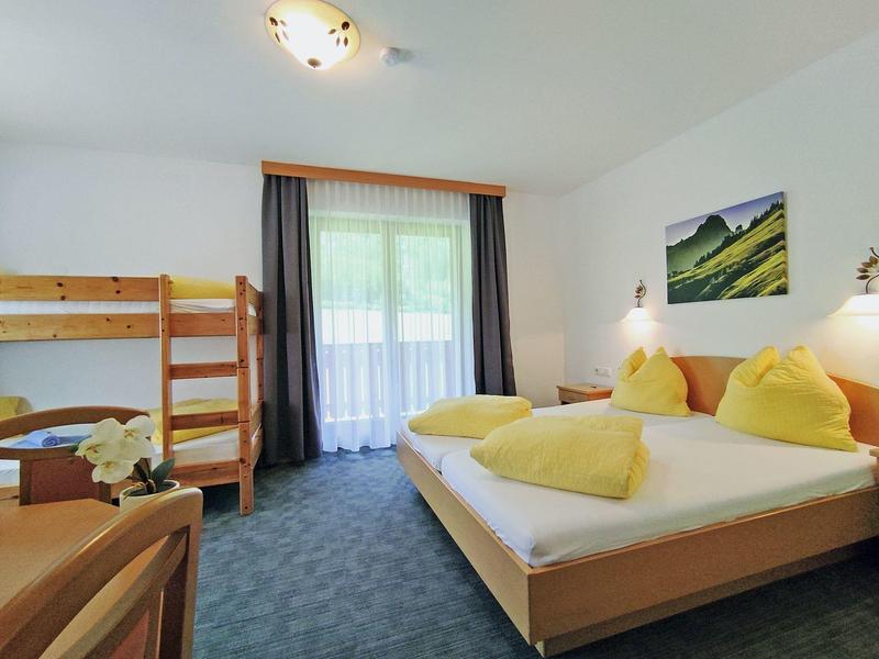 Cozy hotel room with double bed, bunk beds, balcony, and soft natural lighting.