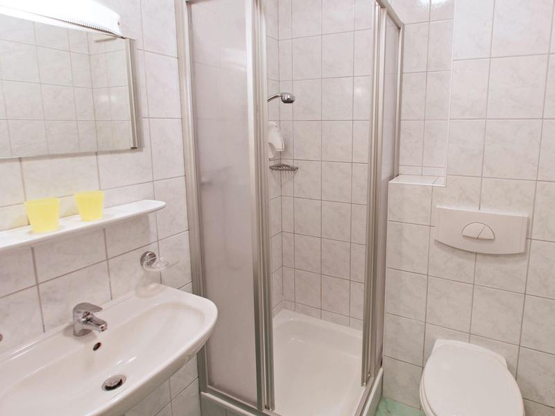 Small hotel bathroom with white tiles, a sink, glass shower, and toilet.