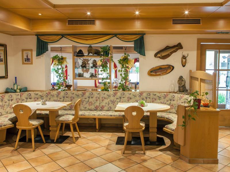 Cozy hotel lounge with wooden chairs, floral sofa, tiled floor, and decorative wall elements.