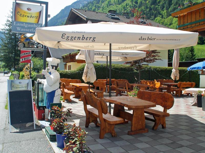 Outdoor wooden tables and benches under large umbrella at a mountain roadside café.
